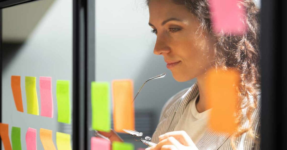 Thoughtful young female boss team leader looking at kanban board