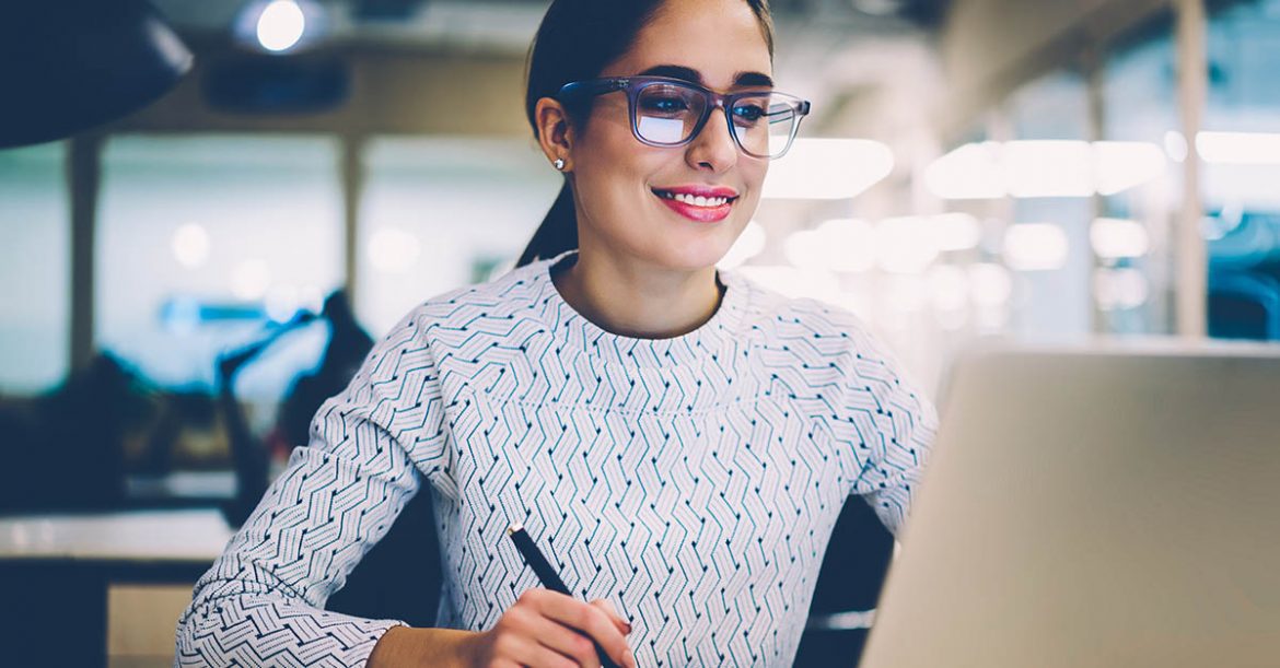 Smiling woman looking at her laptop computer and taking notes