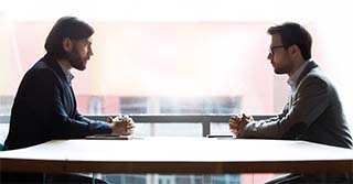 Two businessmen sitting opposite at table, confrontation and negotiation