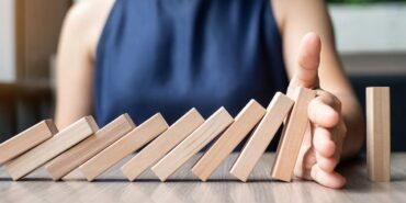 Business woman hand stopping falling wooden dominoes