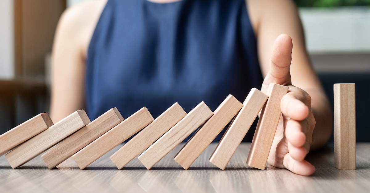 Business woman hand stopping falling wooden dominoes
