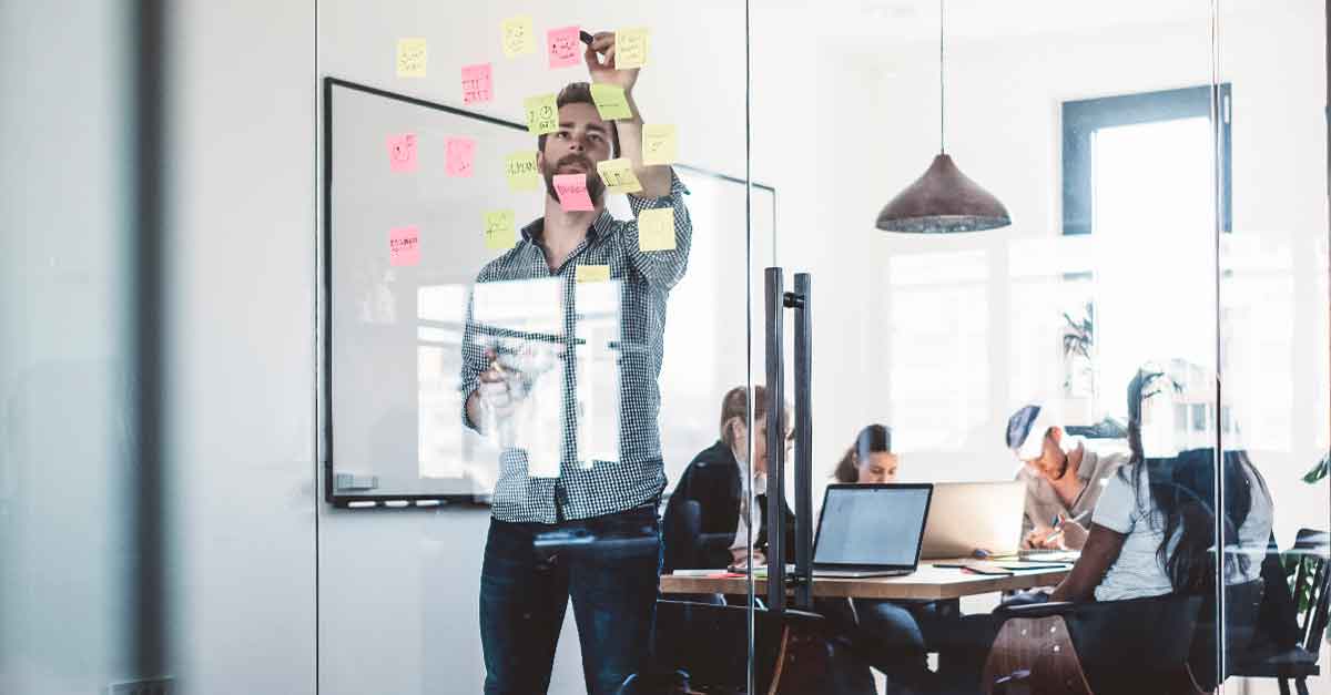 Man standing up and writing on post-it notes in the boardroom with his colleague