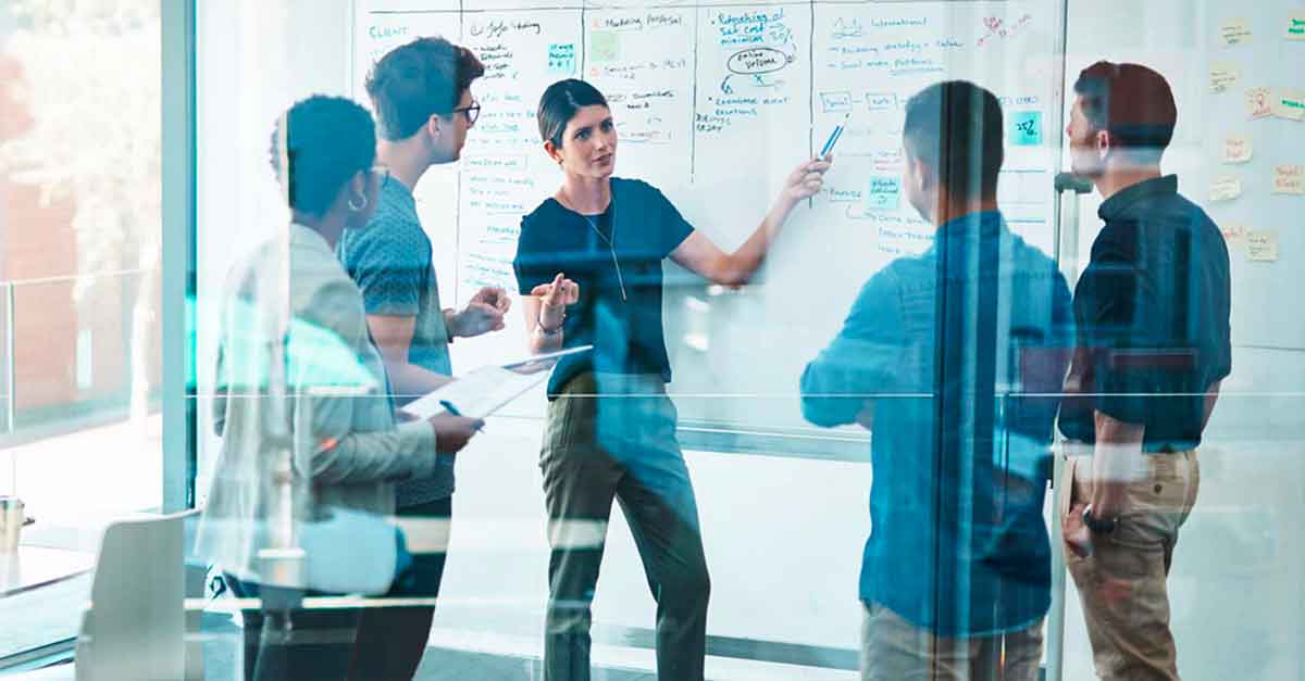 Woman in front of a whiteboard with her colleagues standing around