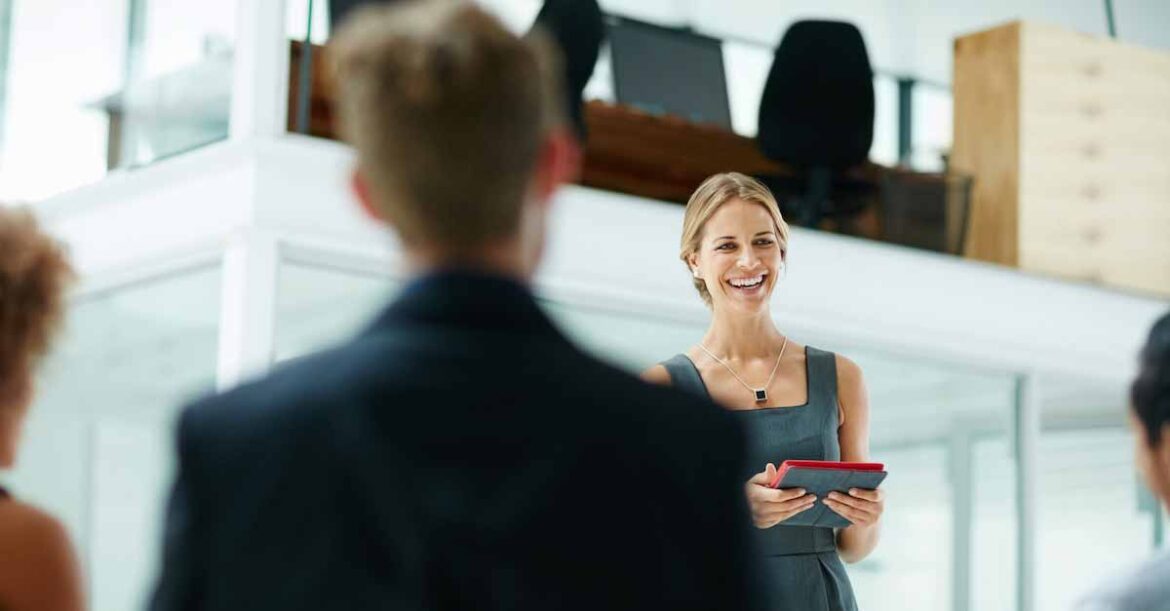 Professional female standing in front of a team in a modern office holding a digital tablet