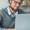 Young male professional sitting at a laptop against a blurred office backdrop