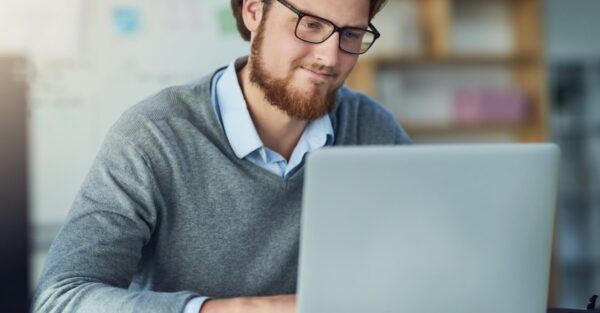 Young male professional sitting at a laptop against a blurred office backdrop