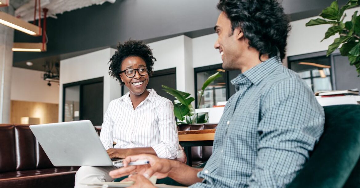 A product manager seated with a laptop chatting with colleague